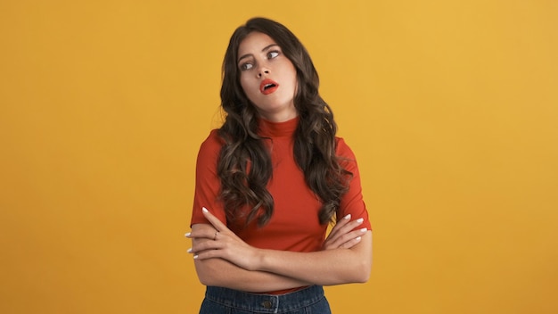Casual verveeld brunette meisje in rode top met handen gekruist vermoeid poseren op camera over gele achtergrond Niet geïnteresseerd expressie