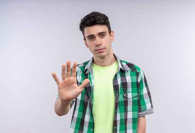 caucasion jonge man met groen shirt met stop gebaar op geïsoleerde witte muur