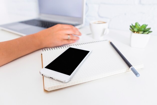 Cellphone, notitieboekje en potlood voor vrouw die laptop met behulp van