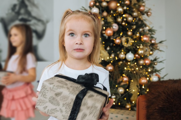 Charmant klein meisje houdt een geschenk vast op een achtergrond van kerstbomen