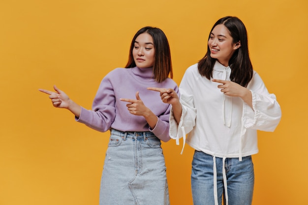 Charmante Aziatische vrouwen in denim-outfits wijzen naar links op de plaats voor tekst op geïsoleerd