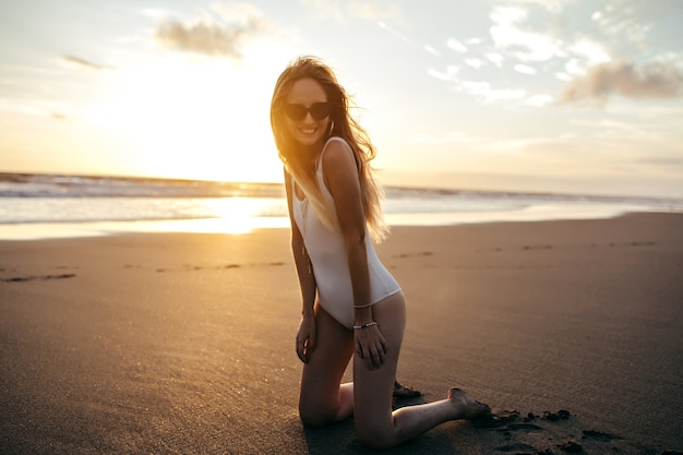 Charmante blanke vrouw in trendy oorbellen poseren aan zandstrand in vakantie.