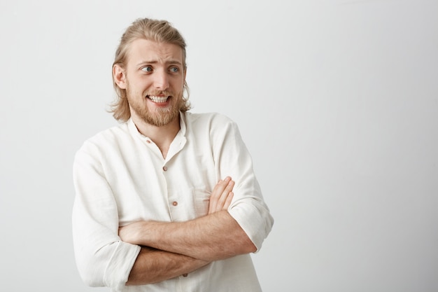 Charmante blonde man met stijlvolle kapsel staan met gekruiste handen