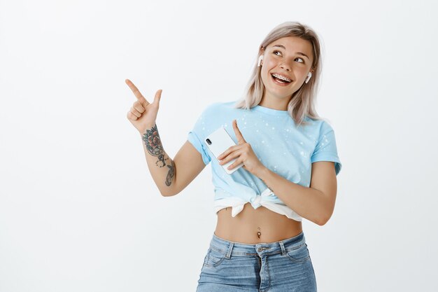 Charmante blonde meisje poseren in de studio met haar telefoon en koptelefoon