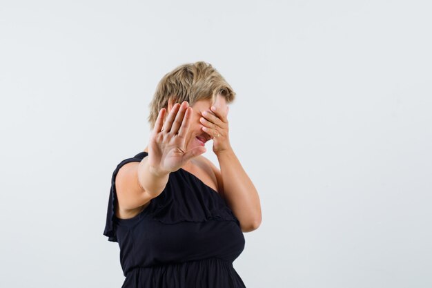 Charmante dame die stopgebaar in zwarte blouse toont en terughoudend kijkt