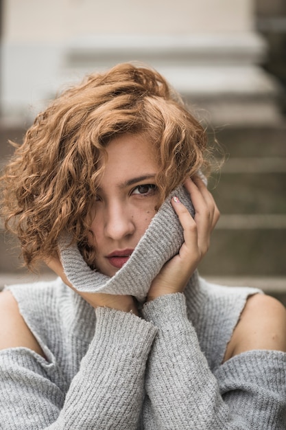 Charmante dame met kort krullend haar dat de kraag van de sweater vasthoudt