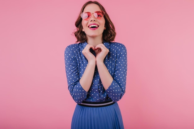 Charmante Europese jonge vrouw in blauwe blouse lachen op pastel achtergrond Enthousiast wit meisje in zonnebril plezier terwijl poseren in studio