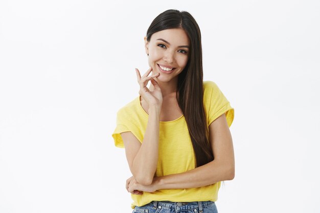 Charmante jonge en vriendelijke donkerharige vrouw in trendy geel t-shirt dat een arm over de borst kruist