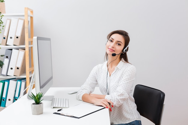 Charmante vrouw bij bureau dat hoofdtelefoon draagt