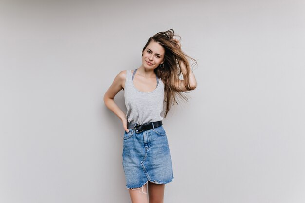 charmante vrouw in denim rok poseren met haar zwaaien. Binnenfoto van slank trendy geïsoleerd meisje.