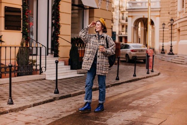 Charmante vrouw in oversized jas met glimlach kijkt in de verte