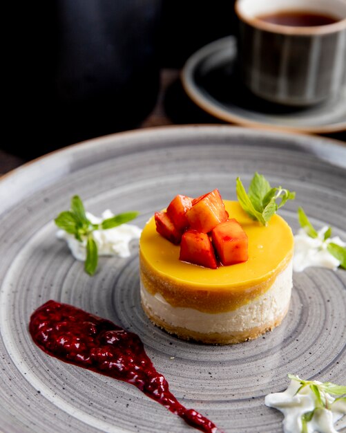 Cheesecake met fruit bovenop geserveerd met bessensaus