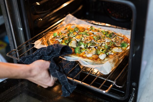 Chef haalt zelfgemaakte biologische volkoren pizza uit de oven, gebruikt tafelkleed om de hand niet te verbranden