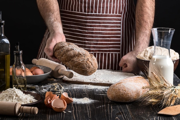 Chef houdt het verse brood in de hand. Man voorbereiding deeg aan tafel in de keuken. Op zwarte achtergrond. Gezond of kookconcept.