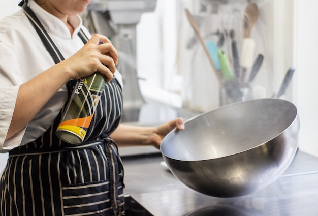 Chef-kok bespuitende olie op een reuzel om kom met een vage achtergrond