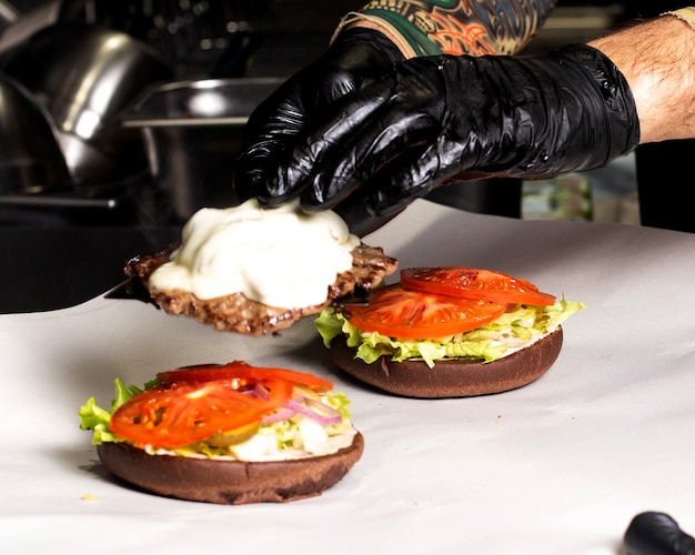 Chef-kok die hamburger met sla van vleescutletcheese tomaten en ui voorbereidt