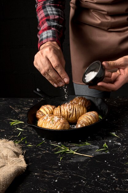 Chef-kok die zout over aardappels in pan bestrooit