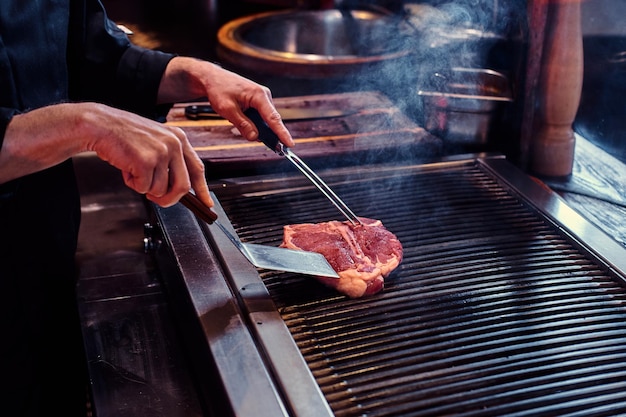 Gratis foto chef-kok draagt uniform koken heerlijke biefstuk op een keuken in een restaurant