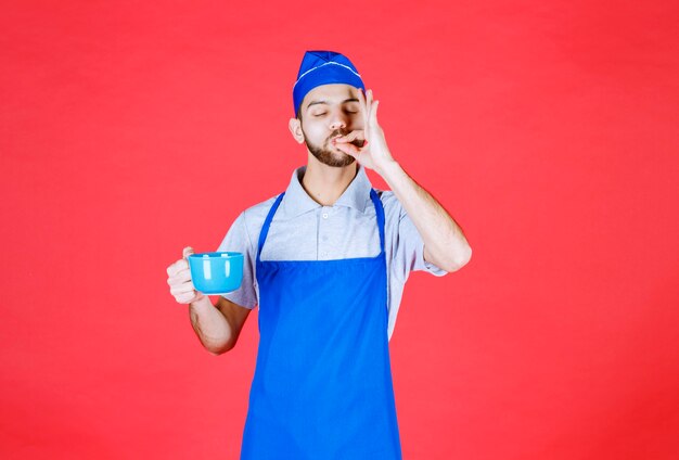 Chef-kok in blauwe schort met een blauwe keramische beker en genietend van de smaak van het product.