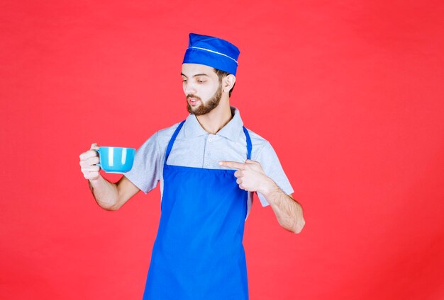 Chef-kok in blauwe schort met een blauwe keramische beker.