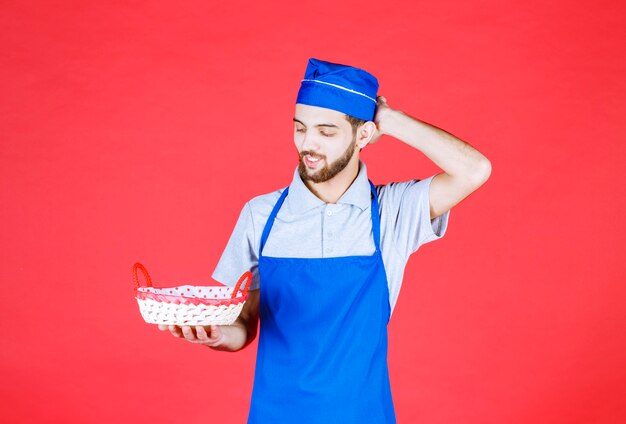 Chef-kok in blauwe schort met een broodmand bedekt met rode handdoek en denken.