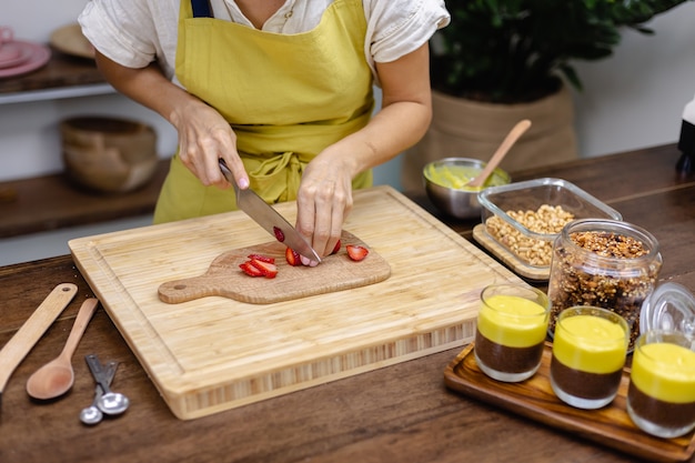 Chia pudding maken. Vrouw gesneden aardbei op een houten bord.