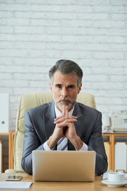 Chief executive officer werkt op laptop met vastberaden blik op de camera