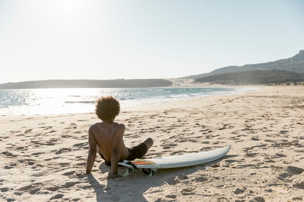 Chillen man zittend op het strand met surfplank