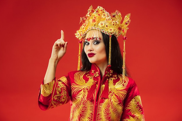 Chinese traditionele bevallige vrouw bij studio over rode achtergrond. mooi meisje dat klederdracht draagt. chinees nieuwjaar, elegantie, genade, performer, performance, dans, actrice, emoties concept