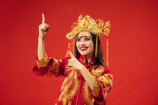 Chinese traditionele bevallige vrouw bij studio over rode achtergrond. Mooi meisje dat klederdracht draagt. Chinees Nieuwjaar, elegantie, gratie, performer, performance, dans, actrice, jurkconcept