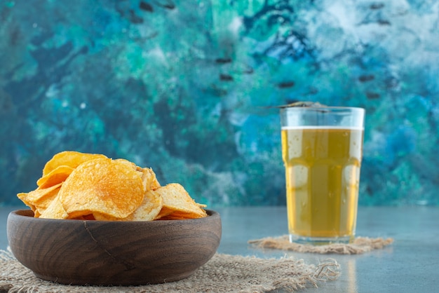 Chips in een kom naast een glas bier, op de marmeren tafel.