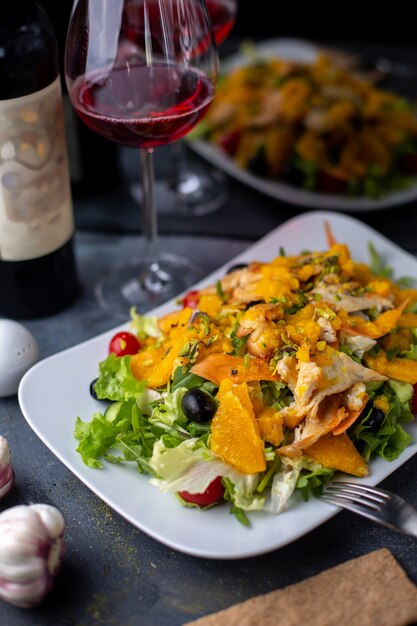 chips oranje salade met gesneden groenten samen met rode wijn op grijze bureau