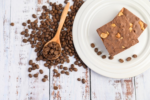 Chocolade brownies op een witte plaat en koffiebonen op een houten lepel.