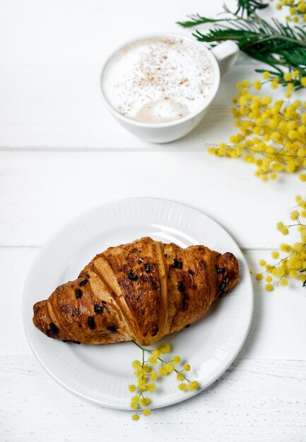 Chocolade croissant en cappuccino versierd met mimosa bloemen op een witte tafel Lente Moederdag concept