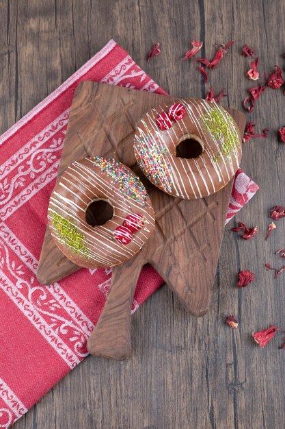 Chocolade donuts op een houten bord met gedroogde rozenblaadjes.