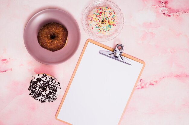 Chocolade en witte donuts met Witboek op klembord over geweven achtergrond