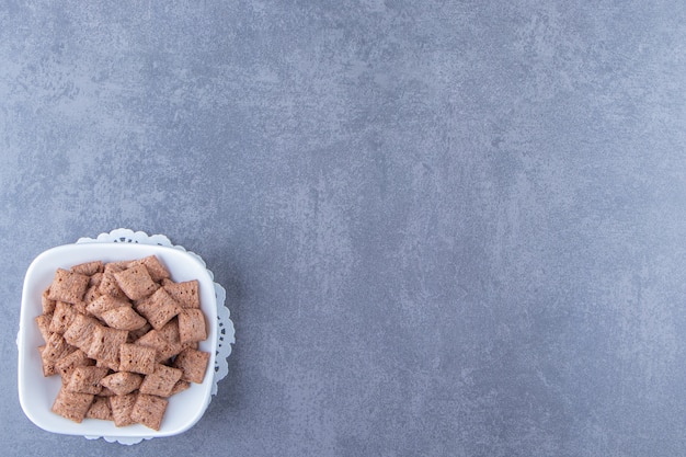 Chocolade maïs pads in kom op een onderzetter, op de blauwe achtergrond.