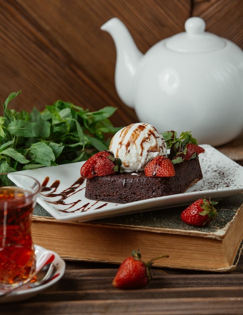 Chocoladebrownie met roomijsbal en aardbeien, en een glas thee