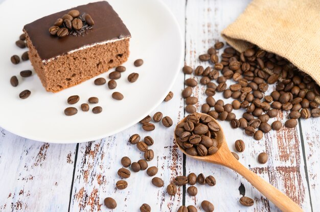 Chocoladecake op een witte plaat en koffiebonen op een houten lepel op een houten lijst.