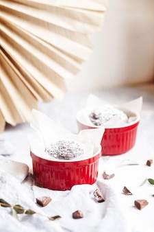 Chocolademuffins in rode kopjes. kleine geglazuurde keramische ramekin met bruine cakes op een grijze en witte achtergrond.