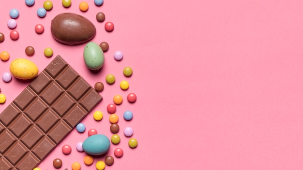Chocoladereep; paaseieren en gem-snoepjes op roze achtergrond