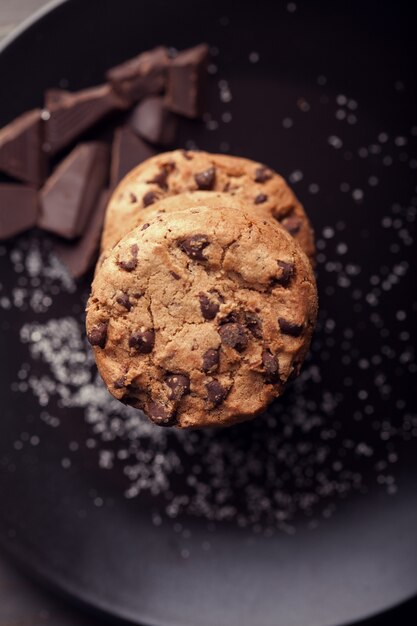 Chocoladeschilferkoekjes op zwarte plaat. Donkere oude houten tafel.