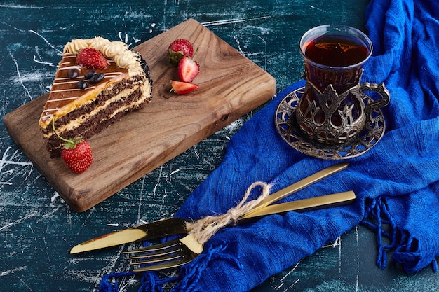 Chocoladetaart geserveerd met aardbeien op blauwe achtergrond met een glas thee.