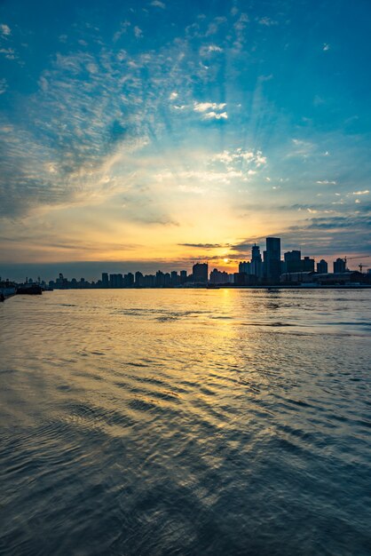 City Skyline By River Against Cloudy Sky