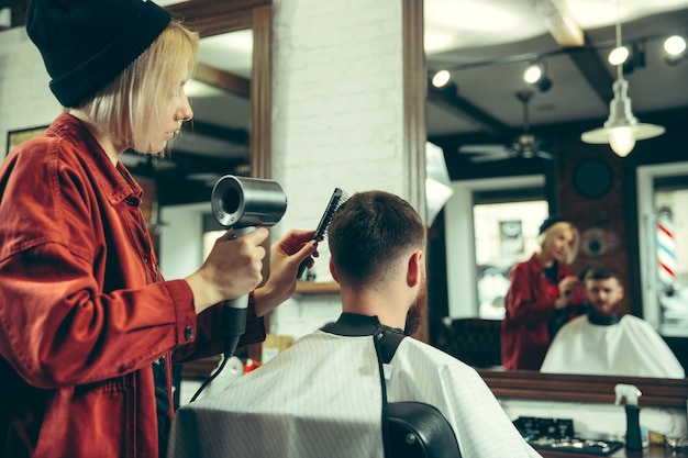 Cliënt tijdens baardscheren in kapperszaak. Vrouwelijke kapper bij salon. Geslachtsgelijkheid. Vrouw in het mannelijke beroep.