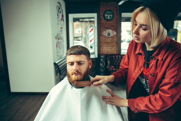 Cliënt tijdens baardscheren in kapperszaak. Vrouwelijke kapper bij salon. Geslachtsgelijkheid