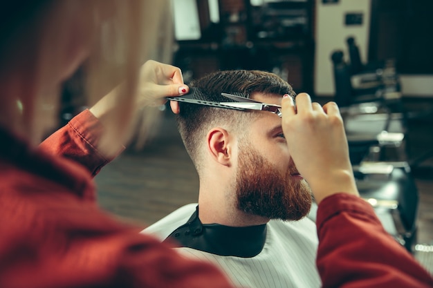 Cliënt tijdens het scheren van de baard in de kapperszaak. Vrouwelijke kapper bij salon. Geslachtsgelijkheid. Vrouw in het mannelijke beroep.