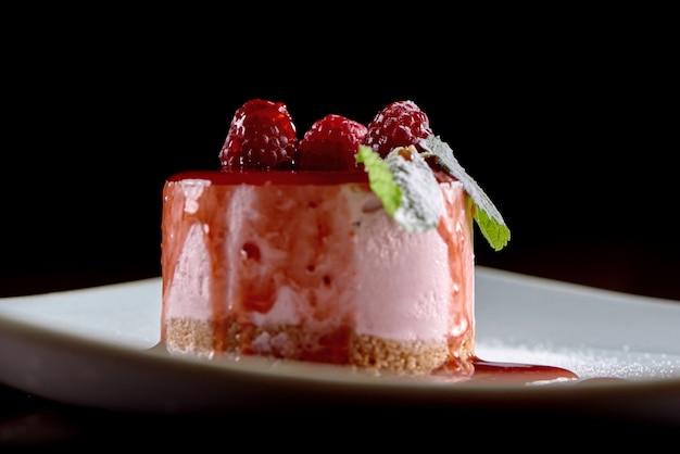 Close-uf een heerlijk soufflé dessert versierd met frambozen en verse muntblaadjes, geserveerd op een witte vierkante plaat. De foto is gemaakt op een zwarte muur. Lekker voor een zoet buffet of catering.