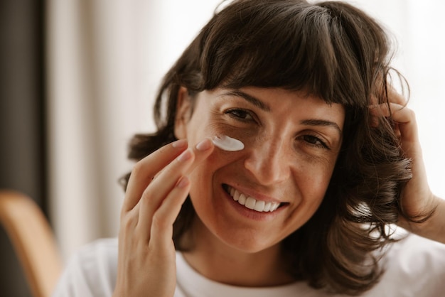 Close-up beeld van gelukkige vrouw producten voor huidcrème kijken naar spiegel