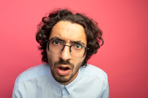 Close-up beeld van onder de indruk jonge knappe man met bril kijken voorzijde geïsoleerd op roze muur